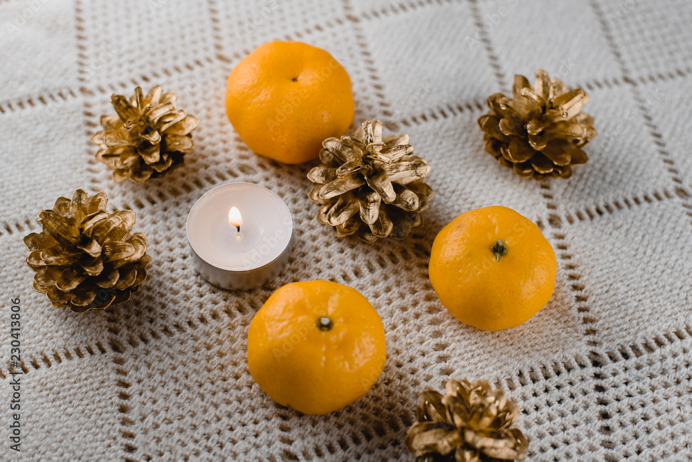 Christmas composition of mandarins , golden cones and a burning decorative candle on a light background