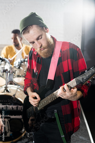 Waist up portrait of contemporary bearded man playing guitar during band rehearsal in studio