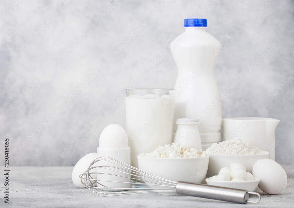 Fresh dairy products on white table background. Plastic bottle and glass of milk, bowl of cottage cheese and baking flour and mozzarella. Eggs and cheese. Steel whisk. Fresh dairy products on white table background. Plastic bottle and glass of milk, bowl of cottage cheese and baking flour and mozzarella. Eggs and cheese. Steel whisk.