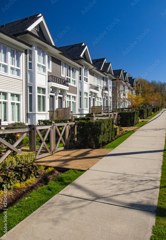 Row of new townhomes in a sidewalk neighborhood. On a sunny day in spring against bright blue sky.