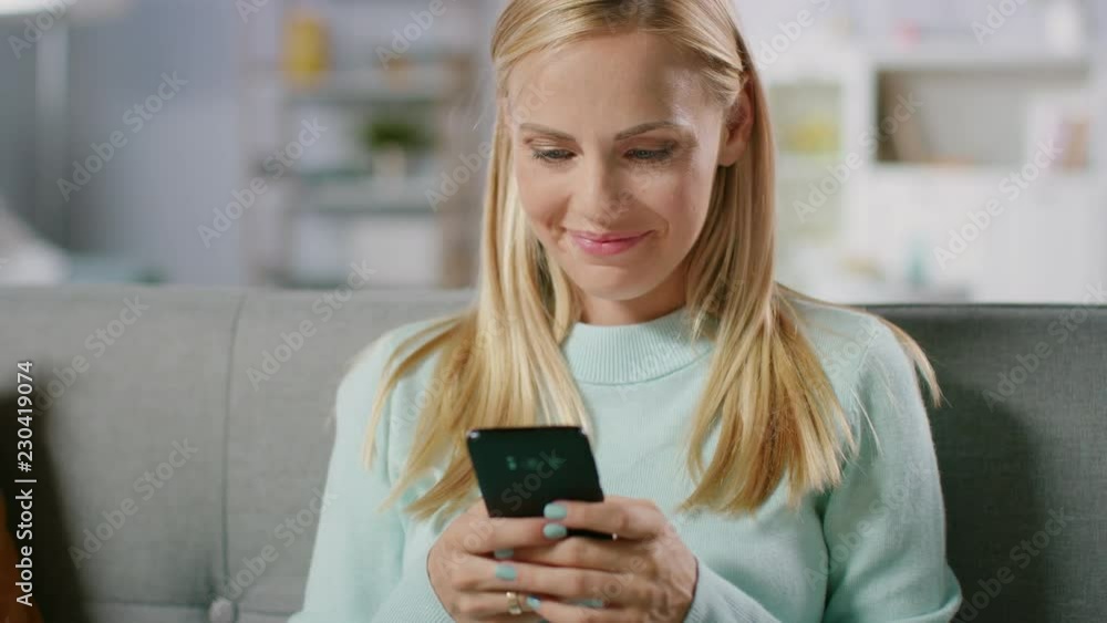 Beautiful Happy Pregnant Woman Sitting on a Couch Browses Through Internet on Smartphone. Future Mom Does Internet Shopping on Smartphone from Home. Beautiful Happy Pregnant Woman Sitting on a Couch Browses Through Internet on Smartphone. Future Mom Does Internet Shopping on Smartphone from Home.