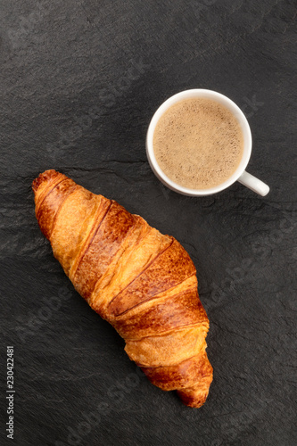 A photo of a croissant with a cup of coffee, shot from the top on a black background with a place for text