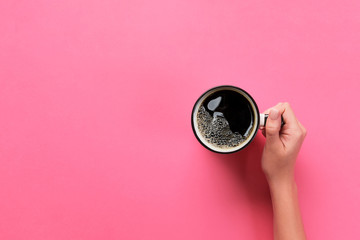 Minimalistic style woman hand holding a cup of coffee on pink background. Flat lay, top view
