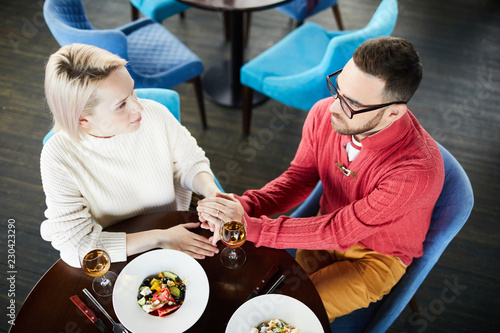 High angle view of loving Caucasian couple sitting at table and holding hands while having romantic date in fine restaurant