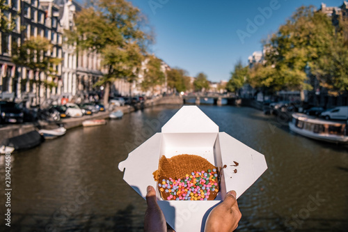 woman hand with Stroopwafel in Amsterdam - typical Dutch food - two circular pieces of waffle filled with caramel-like syrup