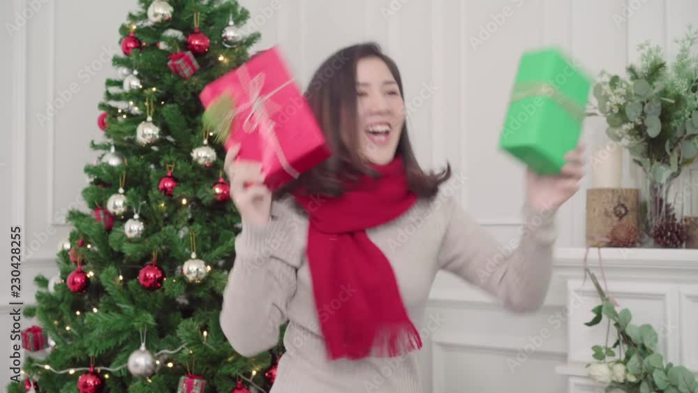 Cheerful happy young Asian woman holding christmas gifts smiling to camera in her living room at home in Christmas Festival. Lifestyle woman celebrate Christmas and New year concept. Cheerful happy young Asian woman holding christmas gifts smiling to camera in her living room at home in Christmas Festival. Lifestyle woman celebrate Christmas and New year concept.
