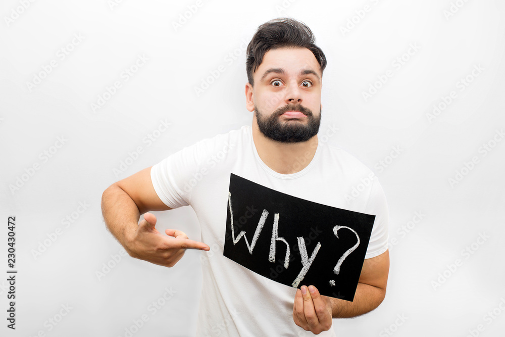 Strange young man showing emotion on face and looking at camera. He holds polate with written word Why. Also he points on it. Isolated on white background. Strange young man showing emotion on face and looking at camera. He holds polate with written word Why. Also he points on it. Isolated on white background.