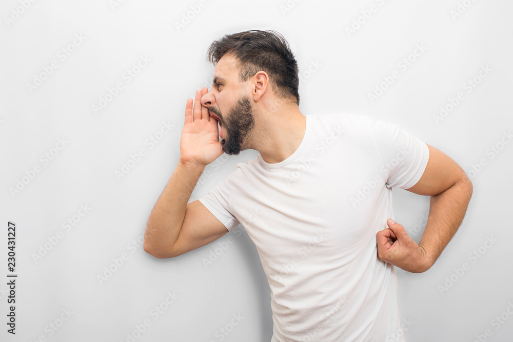 Emotional man expressing his feelings. He screams and yells. Guy coveres mouth with hand from one side. Isolated on white background. Emotional man expressing his feelings. He screams and yells. Guy coveres mouth with hand from one side. Isolated on white background.