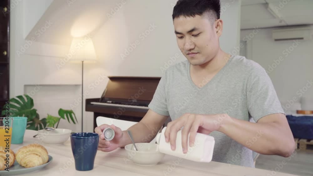 Happy Asian man having breakfast, cereal in milk, bread and drinking orange juice after wake up in the morning. Lifestyle man eating food at home concept. Happy Asian man having breakfast, cereal in milk, bread and drinking orange juice after wake up in the morning. Lifestyle man eating food at home concept.