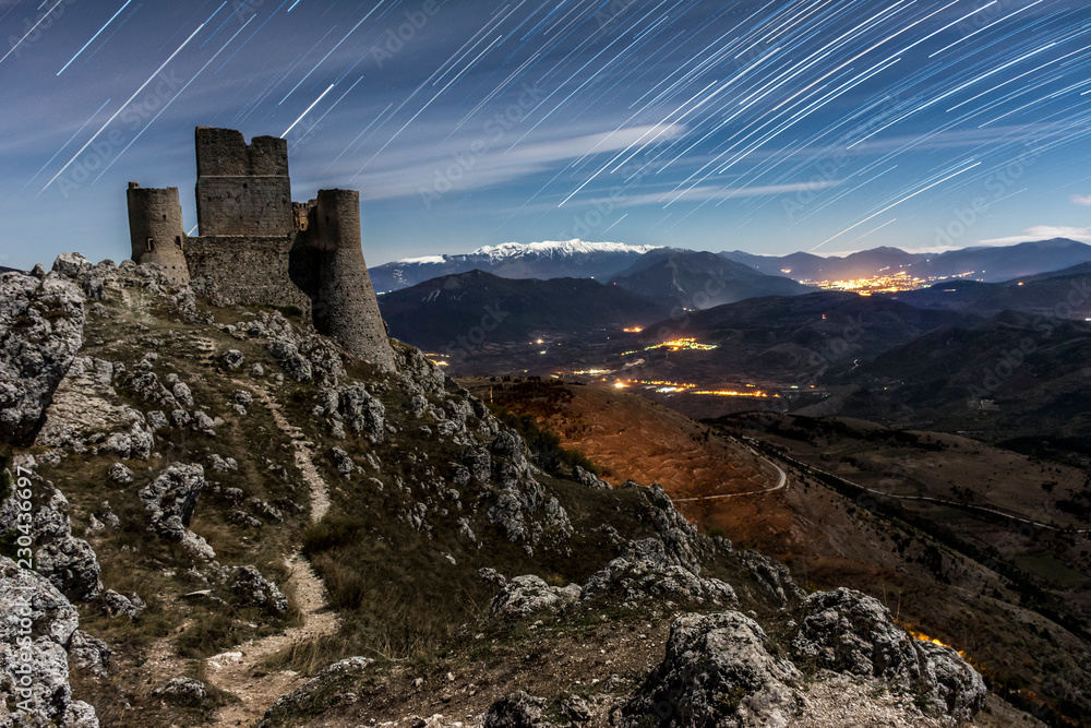 Star trail Rocca Calascio Fortress with moon Light Time, with Shadow - A Medieval Castle Built over the Peak of Mountain in Abruzzo - Italy, Corno Grande background