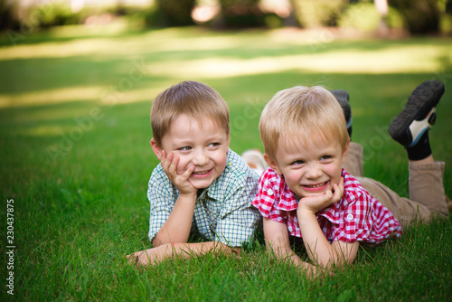 Two brothers lying on the grass in a park outdoors, smiling and