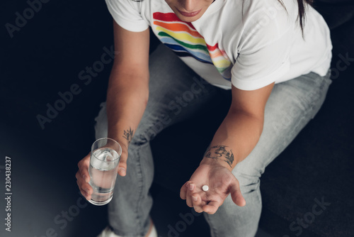 cropped shot of young transgender woman with pill and glass of water sitting on couch
