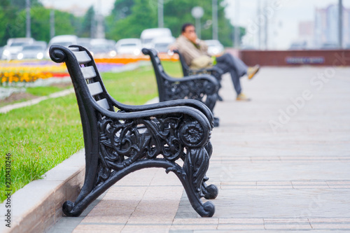 View on a row of benches in a city park with a man sitting in the background in a blur (shallow depth of field) © Mikhail
