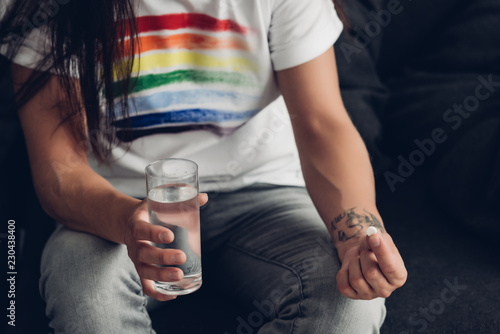 cropped shot of man in t-shirt with pride flag holding glass of water and pill