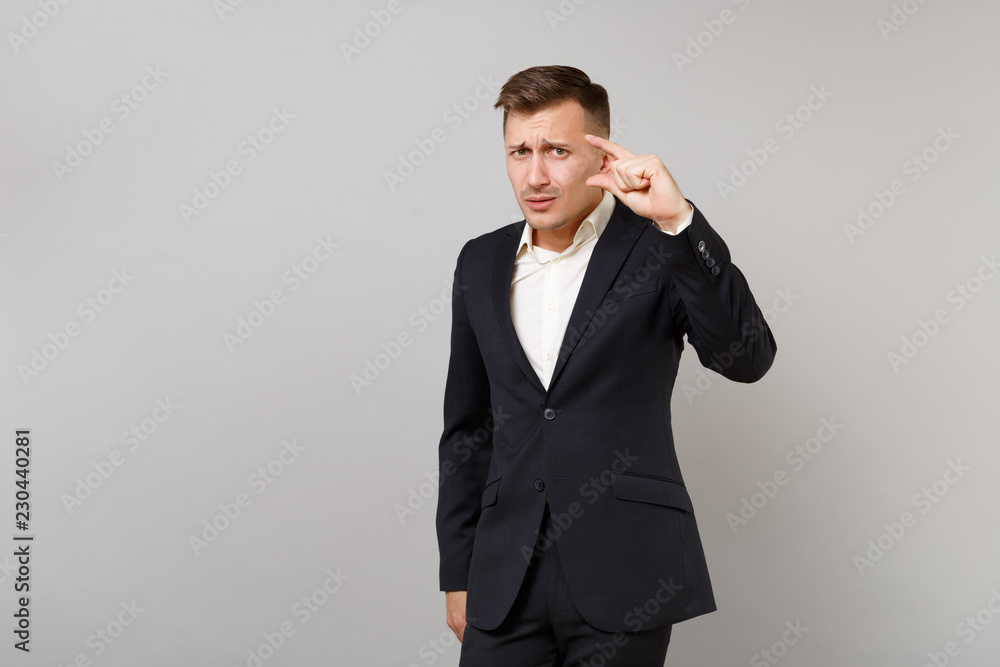 Concerned young business man in classic black suit, shirt gesturing demonstrating size with copy space isolated on grey wall background. Achievement career wealth business concept. Advertising area. Concerned young business man in classic black suit, shirt gesturing demonstrating size with copy space isolated on grey wall background. Achievement career wealth business concept. Advertising area.