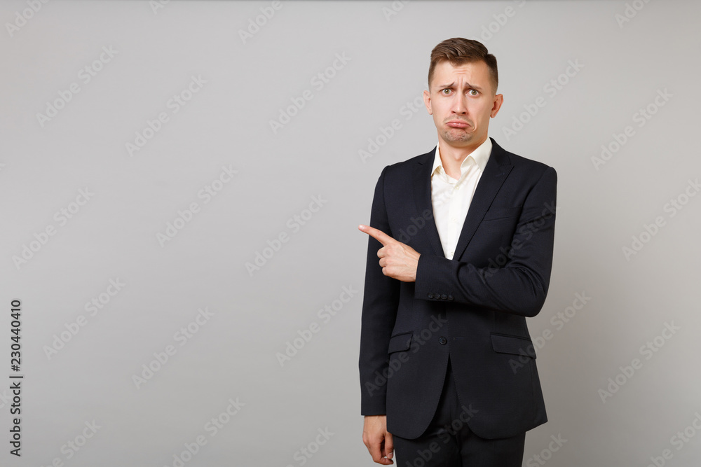 Offended young business man in classic black suit, shirt complaining, pointing index finger aside isolated on grey background in studio. Achievement career wealth business concept. Mock up copy space. Offended young business man in classic black suit, shirt complaining, pointing index finger aside isolated on grey background in studio. Achievement career wealth business concept. Mock up copy space.