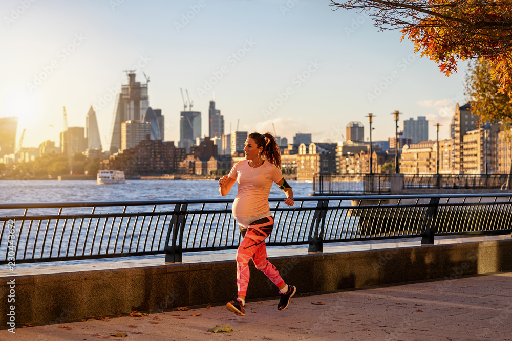 Sportliche, schwangere Frau joggt in London am Ufer der Themse im sonnigen Herbst
