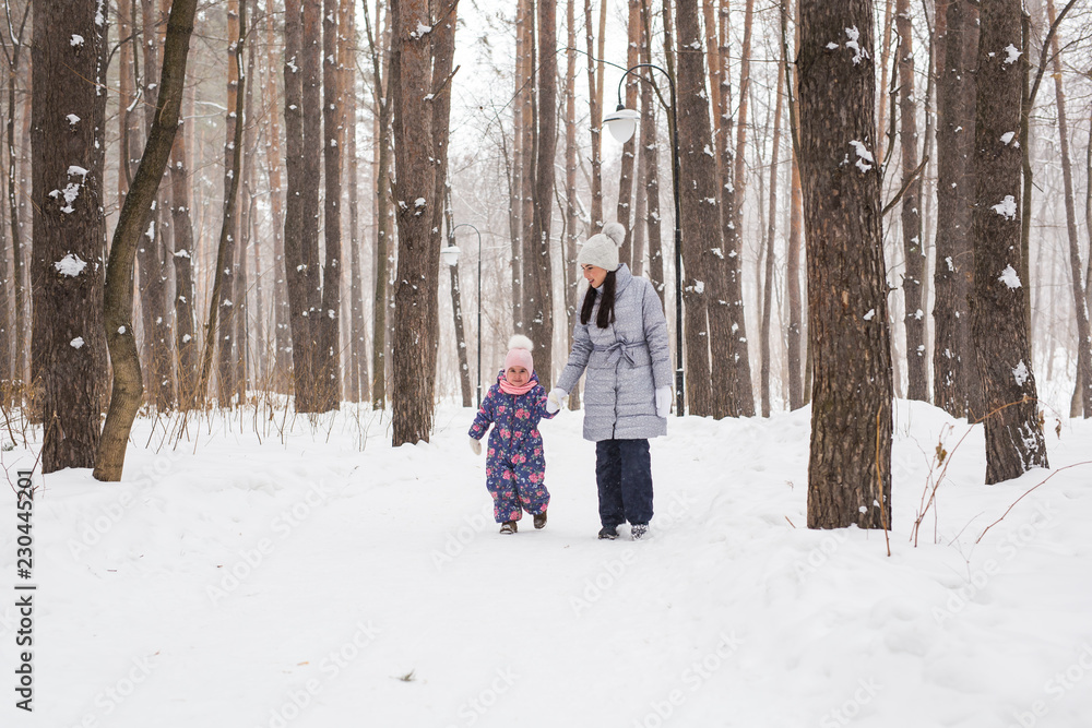 Naklejka premium Winter, childhood and people concept - mother is walking with her little daughter in snowy forest