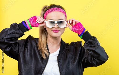 Woman in 1980's fashion with shatter shade glasses on a yellow background