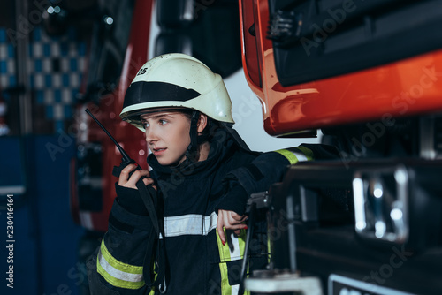 portrait of female firefighter in protective uniform talking into  portable radio set at fire station photo