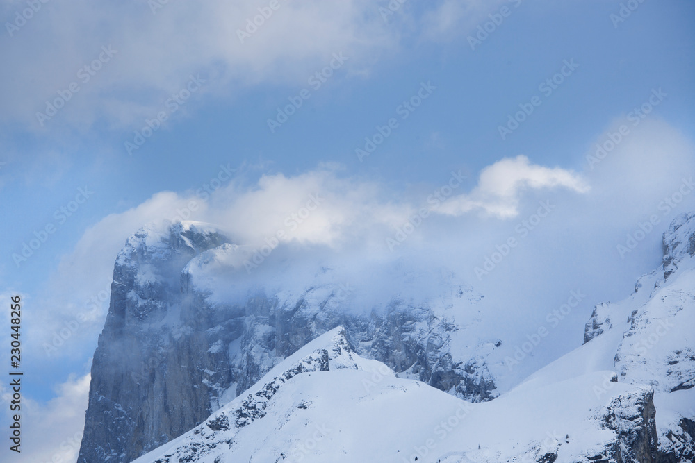 Paysage en hiver à la montagne, campagne, avec la neige blanche qui recouvre la nature et des arbres sauf les sapins. Soleil qui perce entre les nuages au-dessus des vallées enneigées des Alpes