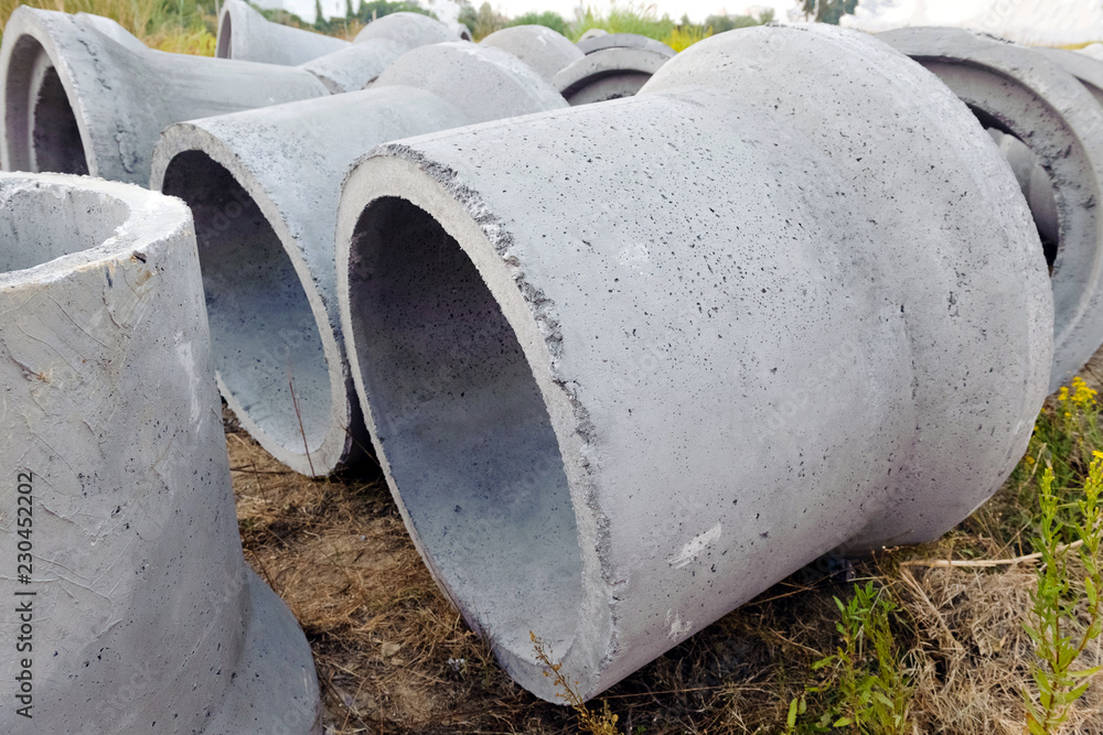 New concrete pipes (rings) are on the ground. In the background are bushes and trees. New concrete pipes (rings) are on the ground. In the background are bushes and trees.