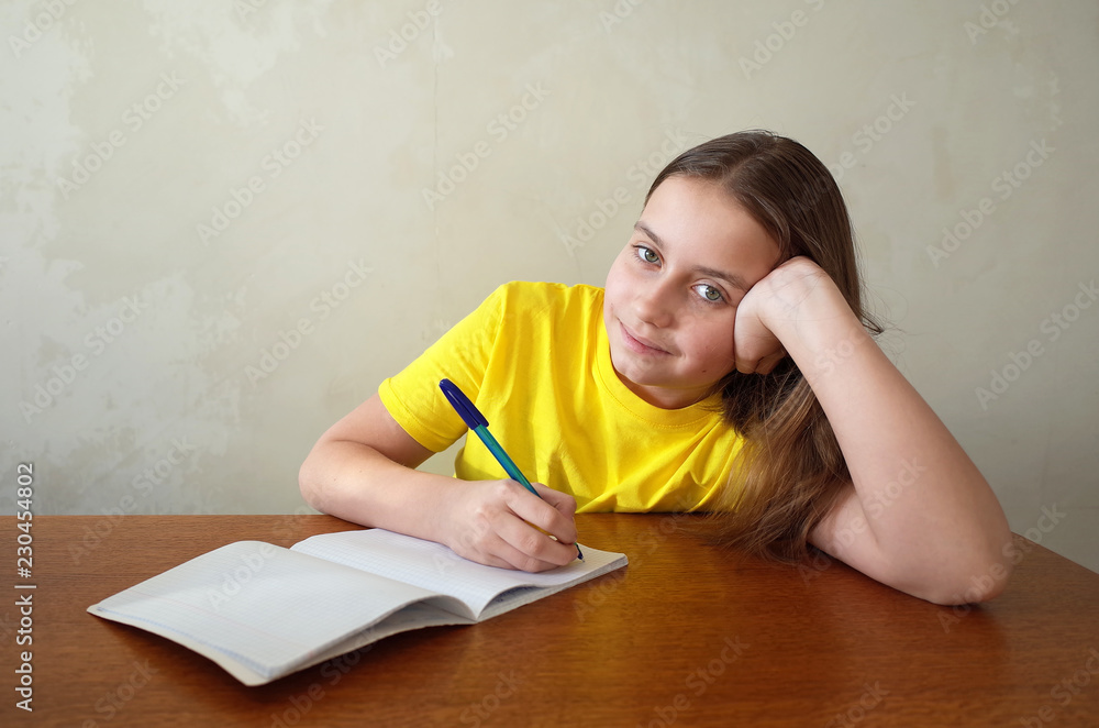 Happy girl writing in notebook placed on wooden desktop with background of grunge grey wall, Children, education and learning concept Happy girl writing in notebook placed on wooden desktop with background of grunge grey wall, Children, education and learning concept