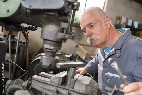 Fotografi elderly worker watches processing of detail on milling machine