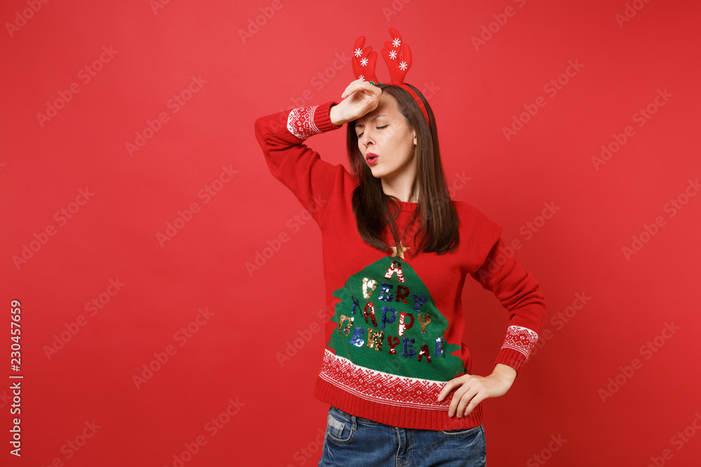 Weary young Santa girl in fun decorative deer horns putting hand on forehead having headache isolated on red wall background. Happy New Year 2019 celebration holiday party concept. Mock up copy space. Weary young Santa girl in fun decorative deer horns putting hand on forehead having headache isolated on red wall background. Happy New Year 2019 celebration holiday party concept. Mock up copy space.