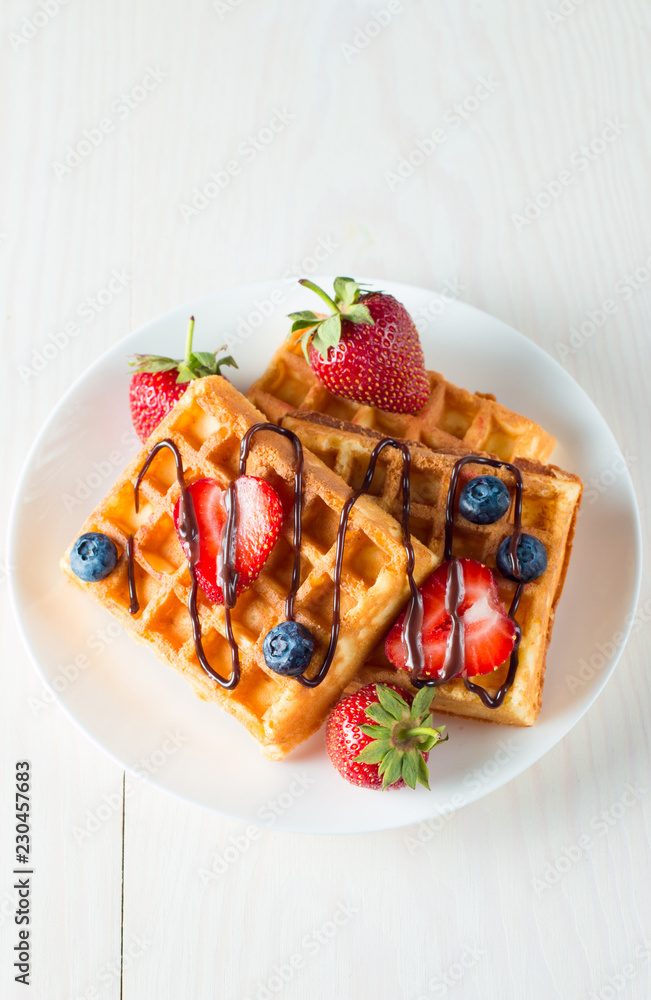 Photo of fresh homemade food made of berry Belgian waffles with honey, chocolate, strawberry, blueberry, maple syrup and cream. Healthy dessert breakfast concept with juice. Photo of fresh homemade food made of berry Belgian waffles with honey, chocolate, strawberry, blueberry, maple syrup and cream. Healthy dessert breakfast concept with juice.