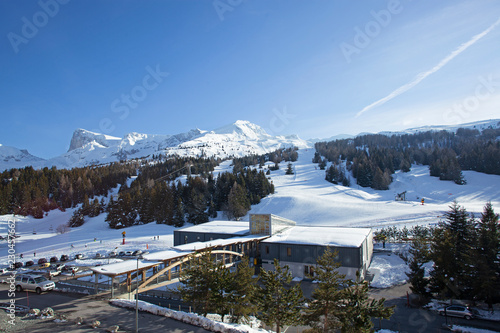 Paysage en hiver à la montagne, campagne, avec la neige blanche qui recouvre la nature et des arbres sauf les sapins. Soleil qui perce entre les nuages au-dessus des vallées enneigées des Alpes