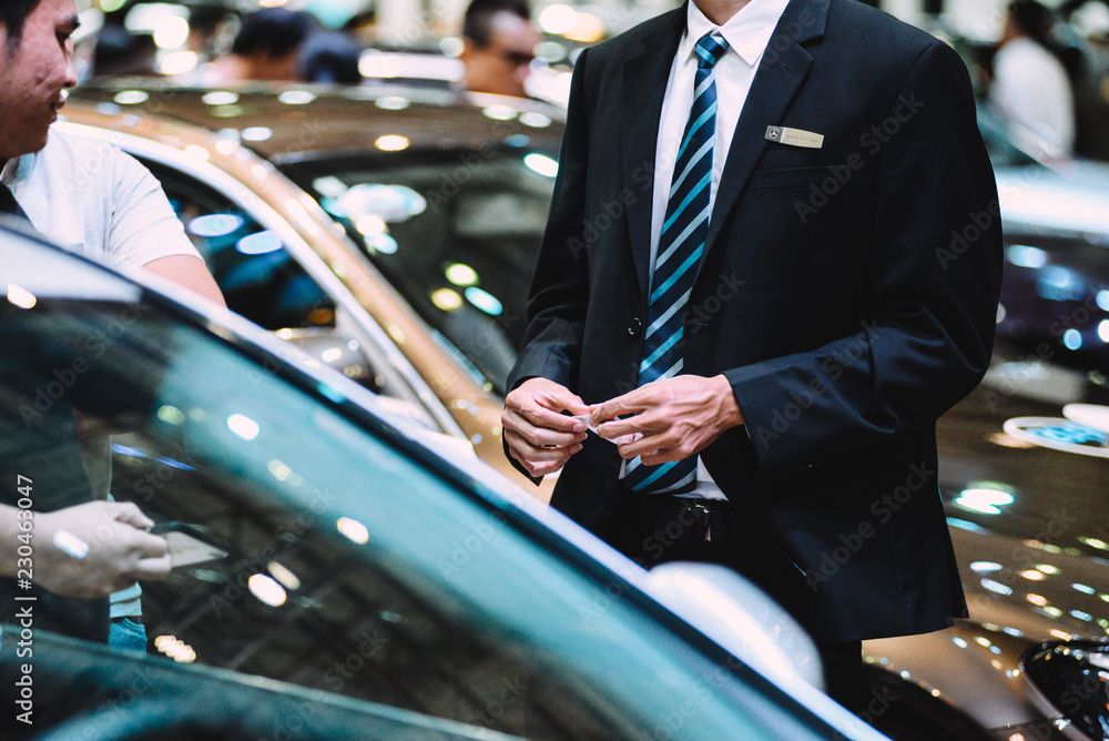 Car dealers are talking to customers and giving business card. He is very professional, wearing a vest and a blue white striped caravat. Car dealers are talking to customers and giving business card. He is very professional, wearing a vest and a blue white striped caravat.