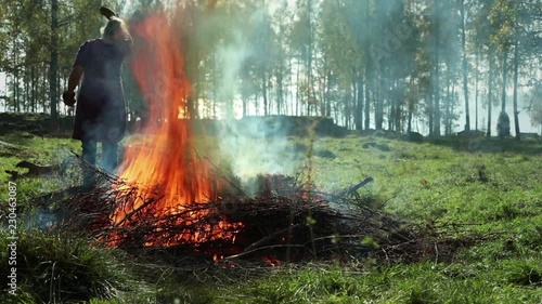 Bonfire in autumn. Bonfire on a meadow to get rid of old bushwood. Woman throwing old branches and leaves on fire. photo