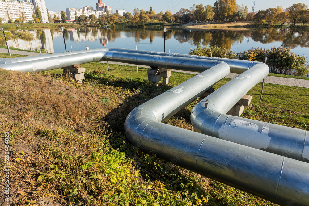 Modern Elevated Heat Pipes. Pipeline above ground, conducting heat to heat city. Urban heat line in metal insulation in residential quarter of city. Open laying on pillars. Municipal heat supply Modern Elevated Heat Pipes. Pipeline above ground, conducting heat to heat city. Urban heat line in metal insulation in residential quarter of city. Open laying on pillars. Municipal heat supply
