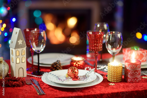 Beautiful table setting for Christmas party or New Year celebration at home. Cozy room with a fireplace and Christmas tree in a background.
