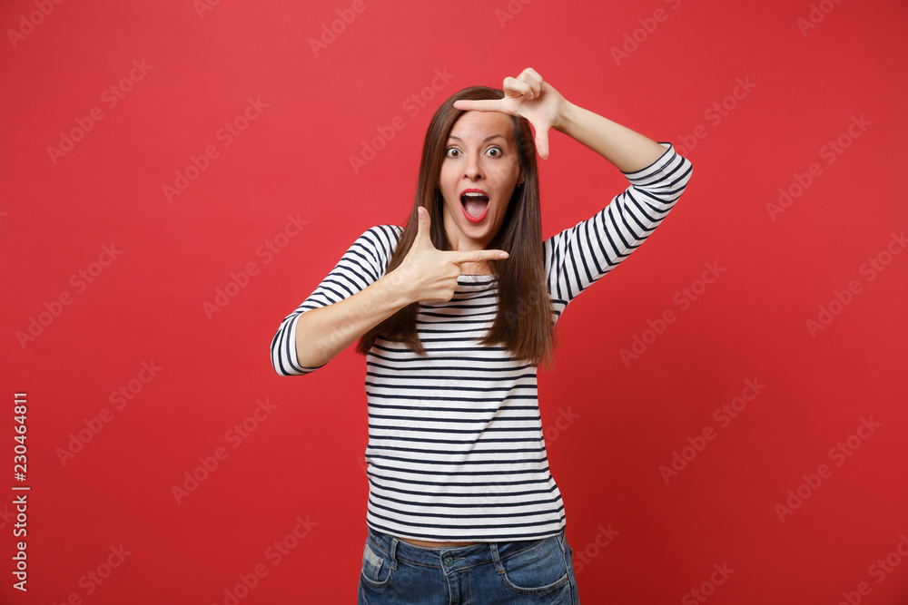 Excited young woman keeping mouth wide open, looking surprised, making hands photo frame gesture isolated on bright red wall background. People sincere emotions, lifestyle concept. Mock up copy space. Excited young woman keeping mouth wide open, looking surprised, making hands photo frame gesture isolated on bright red wall background. People sincere emotions, lifestyle concept. Mock up copy space.