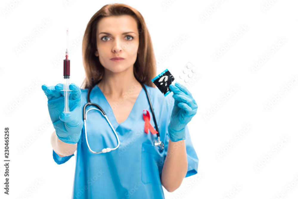 attractive doctor with red ribbon showing syringe with blood and condom with pills isolated on white, world aids day concept attractive doctor with red ribbon showing syringe with blood and condom with pills isolated on white, world aids day concept