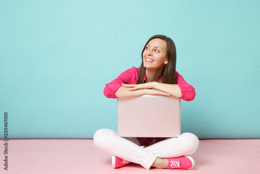 Full length portrait of young woman in rose shirt blouse white pants sitting on floor using laptop pc isolated on pink blue pastel wall background studio. Fashion lifestyle concept. Mock up copy space Full length portrait of young woman in rose shirt blouse white pants sitting on floor using laptop pc isolated on pink blue pastel wall background studio. Fashion lifestyle concept. Mock up copy space
