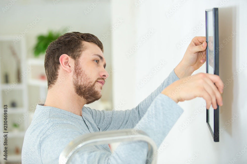 man hanging picture frames on wall at home