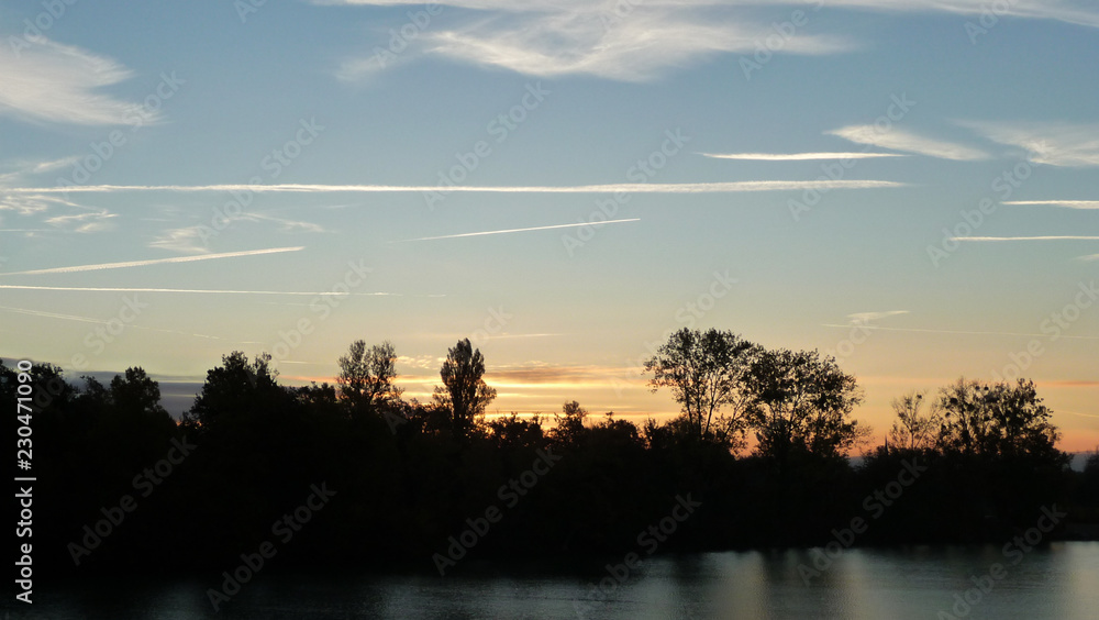 Sunrise on the lake over the forest. Illuminated sky with light clouds.