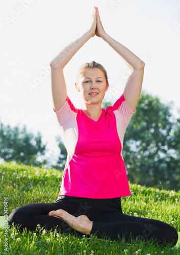 Female 26-32 years old in pink T-shirt is sitting and practising meditation © JackF