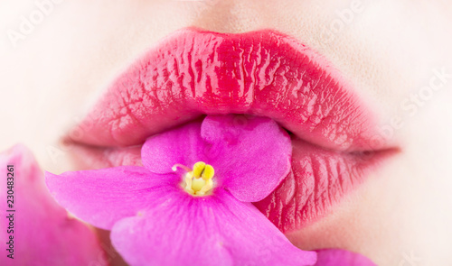 Close-up lips and flower. Close-up beautiful female lip with bright lipgloss makeup. Spa and cosmetics. Lips with flowers, sexy mouth, natural
