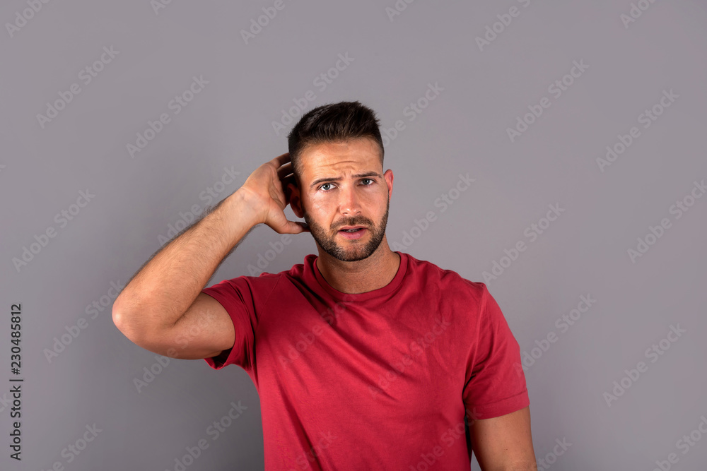 A worried handsome young man in a red tshirt standing in front of a grey background in the studio. A worried handsome young man in a red tshirt standing in front of a grey background in the studio.