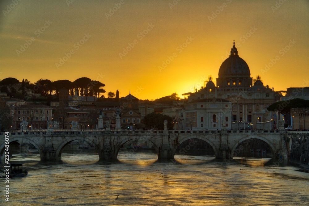 Naklejka premium View of the Vatican over the River Tiber with the sun setting behind St. Peter’s Basilica.
