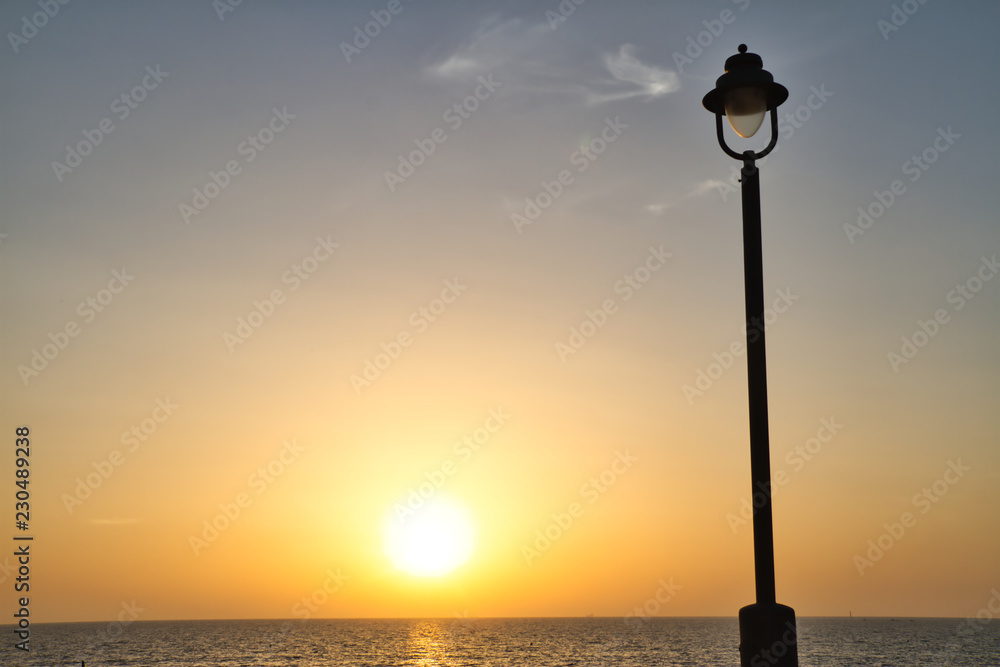 The sun setting over the Atlantic Ocean with a light post in the foreground.