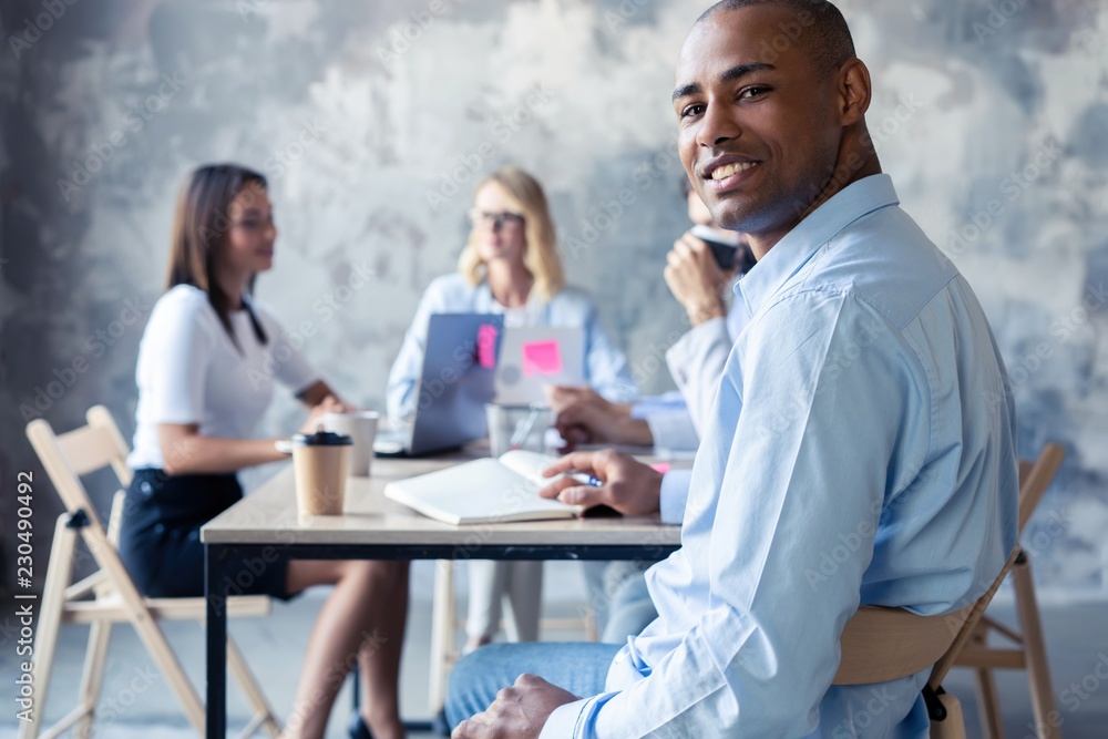 Portrait of smiling African American business man with executives working in background. Portrait of smiling African American business man with executives working in background.