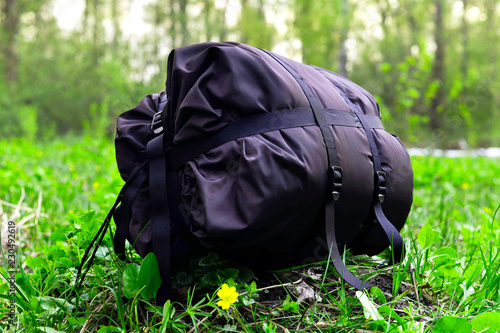 Sleeping tourist bag black rolled up in the woods on a background of grass.