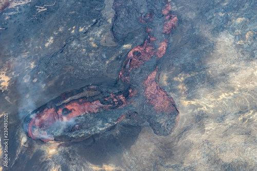 Active fissure in Leilani Estates on Hawaii's Big island. Surrounded by recent lava flow, red magma is visible; white volcanic gas rises from the vents.  photo
