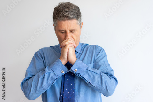Stressed business leader having troubles. Focused Caucasian man in formal shirt and tie praying with closed eyes and clasped hands. Pray or problem concept