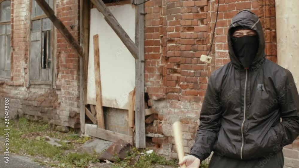 Hooliganin black mask and jacket with hood holds in baseball bat on street Hooliganin black mask and jacket with hood holds in baseball bat on street